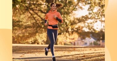 happy brunette woman running for exercise on park trail on sunny autumn day