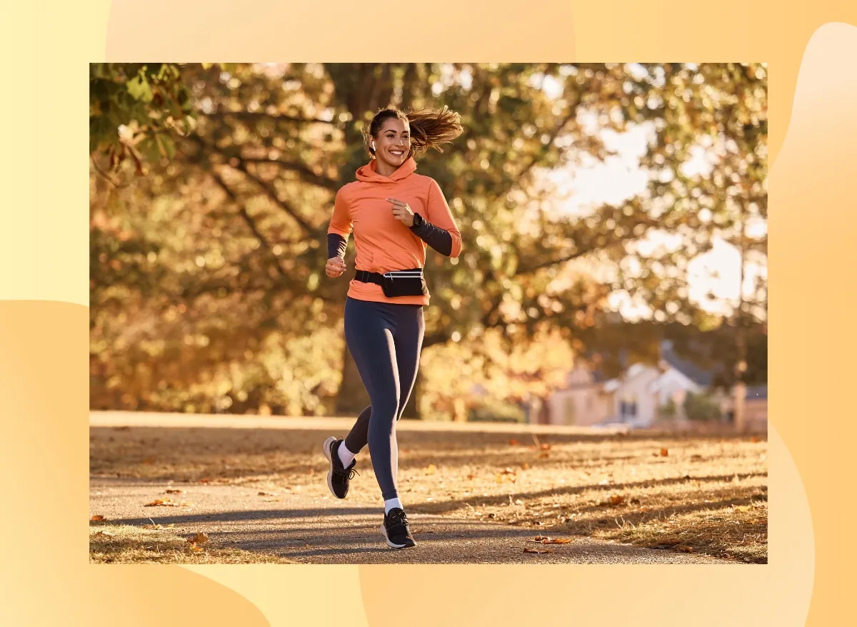 happy brunette woman running for exercise on park trail on sunny autumn day