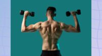 back view of fit, muscular shirtless man doing dumbbell press exercise, lifting dumbbells, in front of greenish blue backdrop