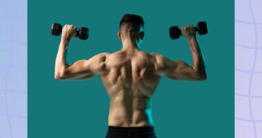 back view of fit, muscular shirtless man doing dumbbell press exercise, lifting dumbbells, in front of greenish blue backdrop