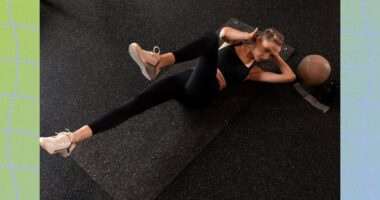 fit woman doing bicycle crunches on black yoga mat in dark gym setting