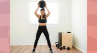 fit, focused woman doing a slam ball front slam exercise in bright workout room