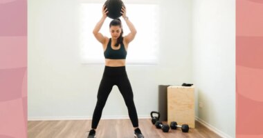 fit, focused woman doing a slam ball front slam exercise in bright workout room