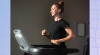 fit, focused brunette woman in black t-shirt and leggings walking on treadmill