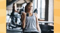 focused, middle-aged woman lifting weights seated at a workout bench in a gym