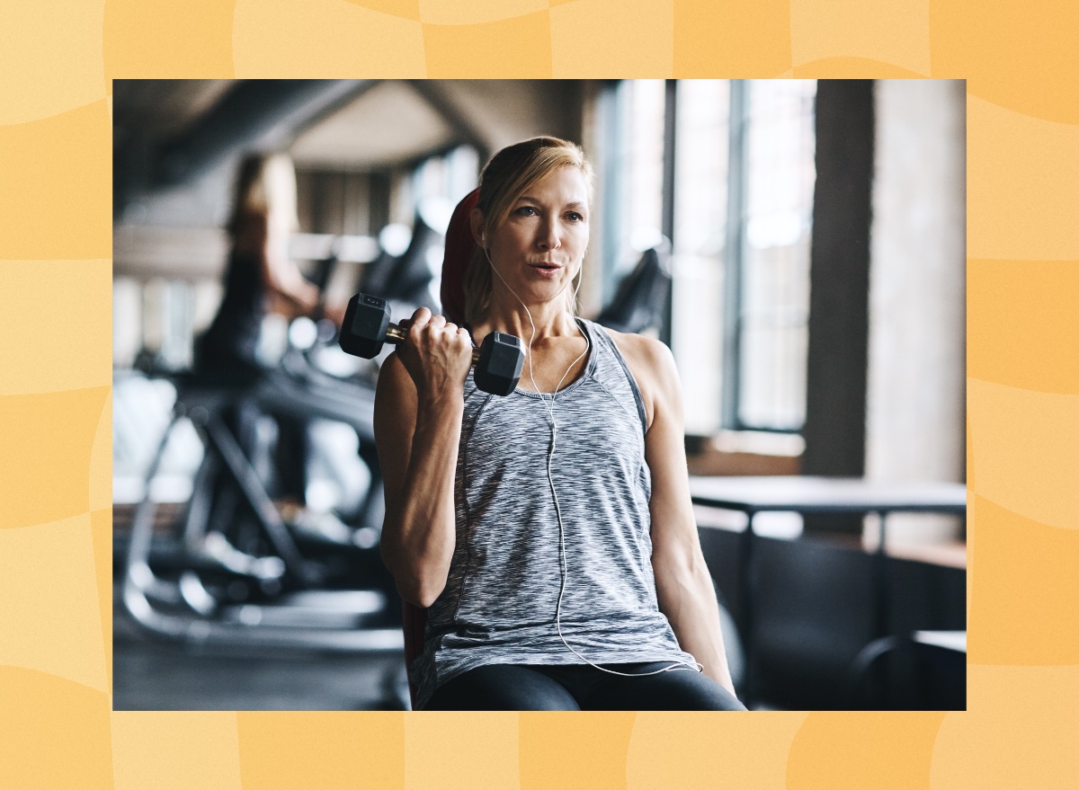 focused, middle-aged woman lifting weights seated at a workout bench in a gym