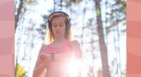 blonde woman wearing headphones and pink sports bra checking fitness tracker while on a run through the woods on sunny day