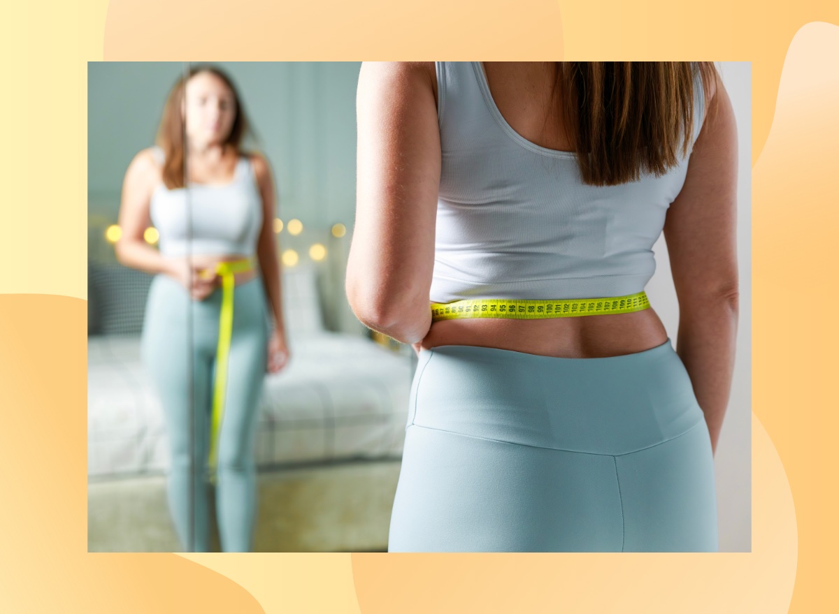 close-up of woman in athletic outfit measuring herself and looking in the mirror in her bedroom