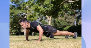 fit, focused middle-aged man doing pushups outdoors on the grass on a sunny day