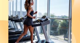 fit woman running on treadmill at the gym in front of floor to ceiling windows