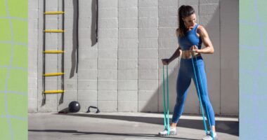 fit woman training with resistance bands, doing arm exercises outdoors