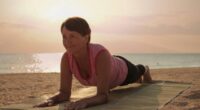 mature woman doing beach yoga plank on straw mat at sunrise or sunset