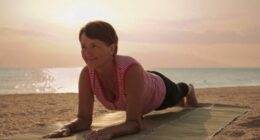 mature woman doing beach yoga plank on straw mat at sunrise or sunset