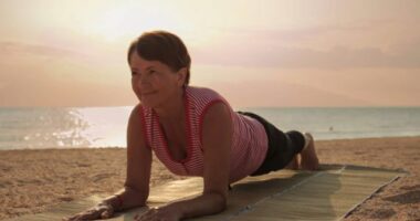 mature woman doing beach yoga plank on straw mat at sunrise or sunset