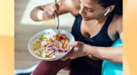 close-up of fitness woman eating healthy lunch while sitting next to exercise ball in bright living space