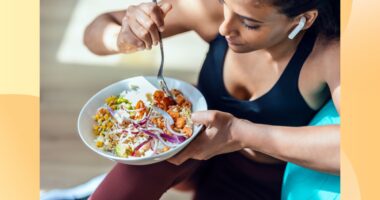 close-up of fitness woman eating healthy lunch while sitting next to exercise ball in bright living space