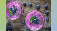 blueberry chia smoothie in two cups on wooden table, surrounded by fresh blueberries