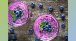 blueberry chia smoothie in two cups on wooden table, surrounded by fresh blueberries