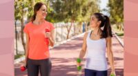 two fit female friends walking on track with dumbbells for exercise