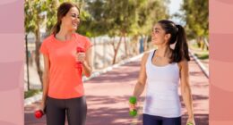 two fit female friends walking on track with dumbbells for exercise