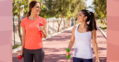 two fit female friends walking on track with dumbbells for exercise