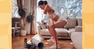 fit, determined brunette woman doing resistance band squats in bright living room