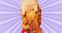 A chicken tender from KFC, dripping with sauce and held in a woman