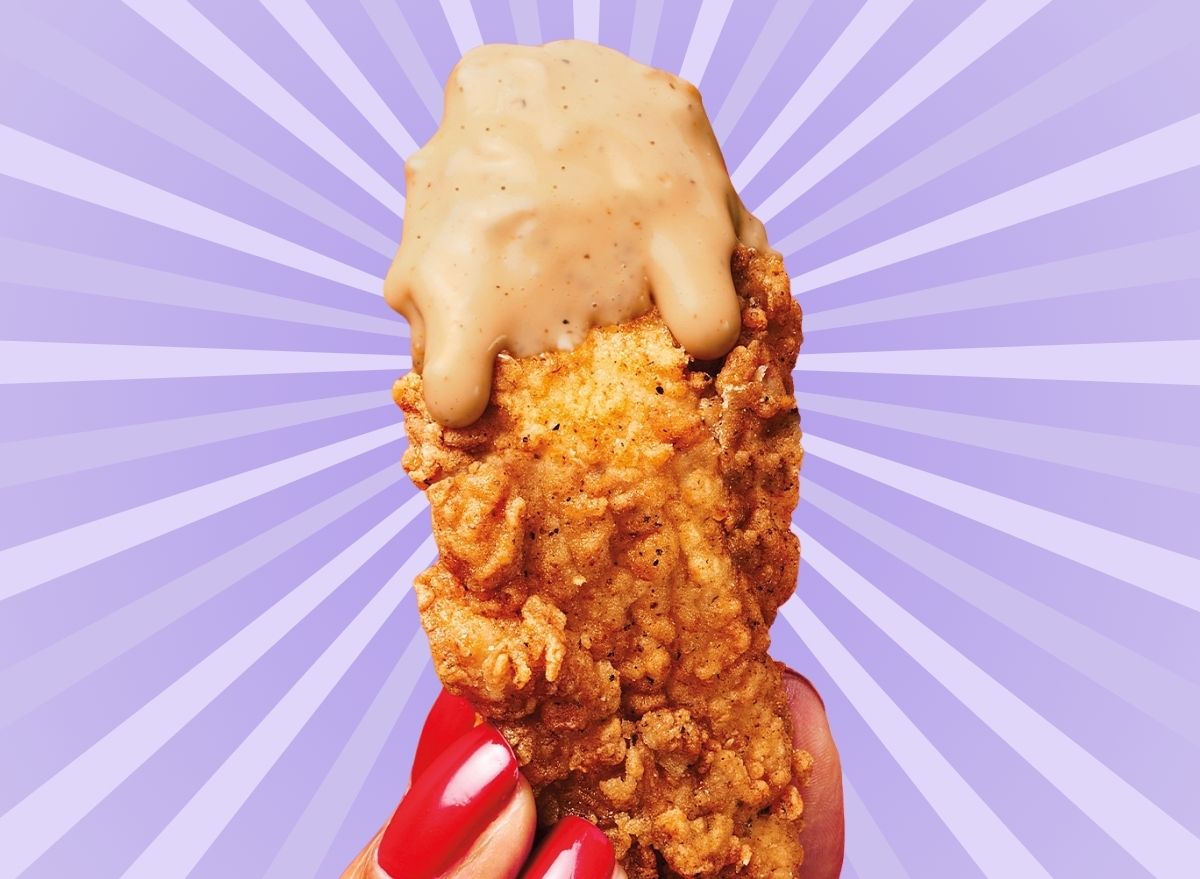 A chicken tender from KFC, dripping with sauce and held in a woman