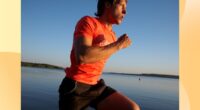 fit, focused man running alongside lake beach at sunset