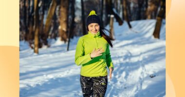 happy brunette woman running in the snow for exercise on winter day