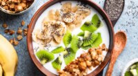 bowl of yogurt with banans chia seeds kiwis nuts and granols