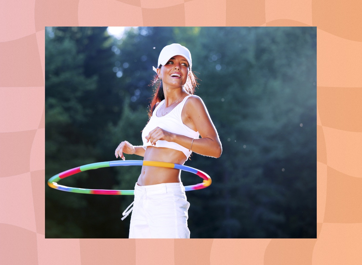 fit brunette woman doing a hula hoop workout outdoors