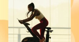 fit woman doing indoor cycling workout in front of floor-to-ceiling windows