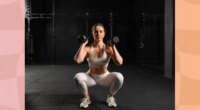 fit, focused woman doing squat to press exercise in dark gym