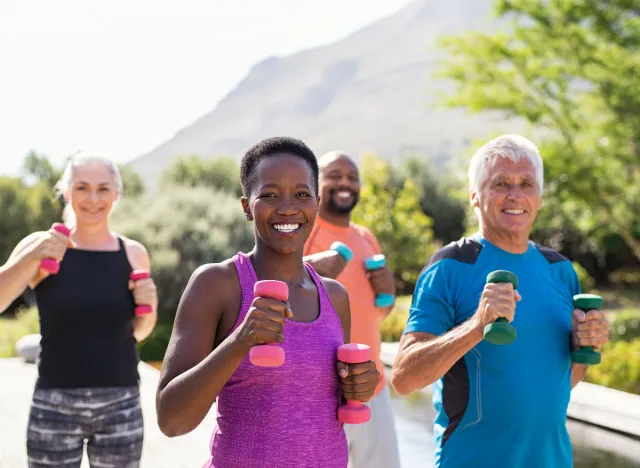 group of active people using dumbbells during walking workout outside