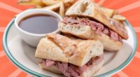 A classic French dip sandwich with fries and au jus set against a vibrant background