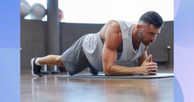 muscular, determined man holding a forearm plank on yoga mat in workout space