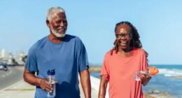 happy mature couple laughing and walking for exercise by the beach