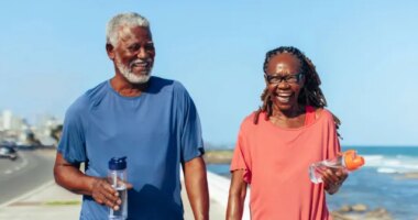 happy mature couple laughing and walking for exercise by the beach