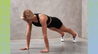 fit blonde woman doing high plank exercise in front of gray wall