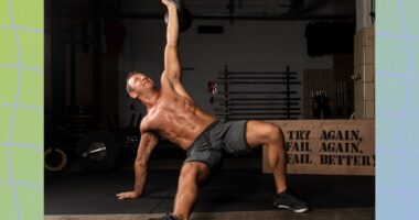 fit, muscular, shirtless man doing Turkish get-up exercise in dark gym set-up