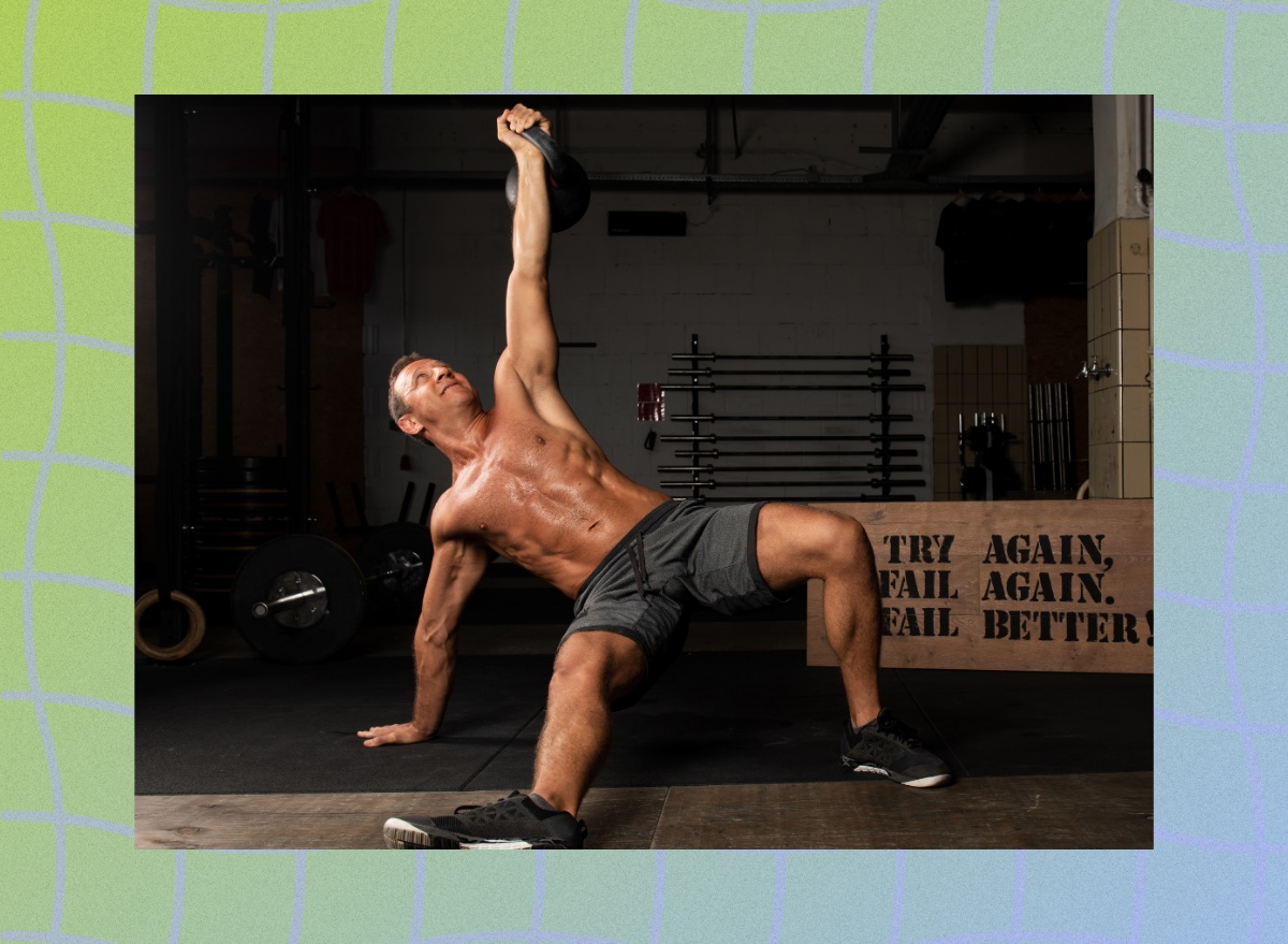 fit, muscular, shirtless man doing Turkish get-up exercise in dark gym set-up