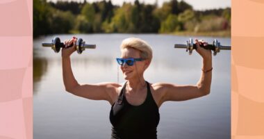 fit, mature blonde woman lifts dumbbells by a lake on a sunny day