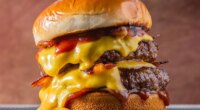 double meet Burger with melting cheddar cheese and bacon centralized on a gray surface and brown background.