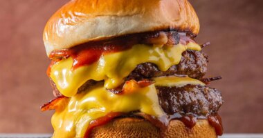 double meet Burger with melting cheddar cheese and bacon centralized on a gray surface and brown background.