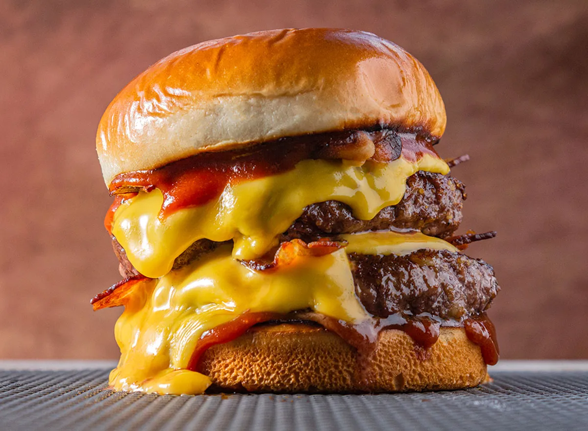 double meet Burger with melting cheddar cheese and bacon centralized on a gray surface and brown background.