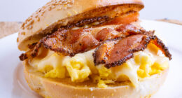 breakfast sandwich of toasted sesame bagel, slab bacon, egg and melted cheese.