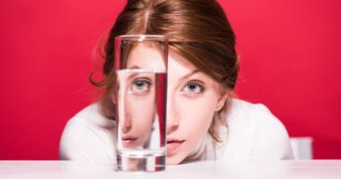 young woman looking through glass of water