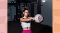 fit, focused woman doing kettlebell swing in dark gym