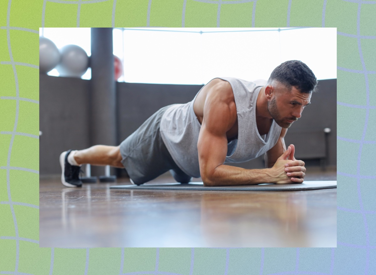 fit, muscular man holding a forearm plank on workout mat at the gym